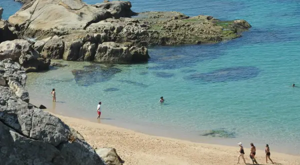 Słoneczne kadyks plaże z turkusową wodą i skalistymi formacjami. Kilka osób cieszy się kąpielą i spacerem po piasku.