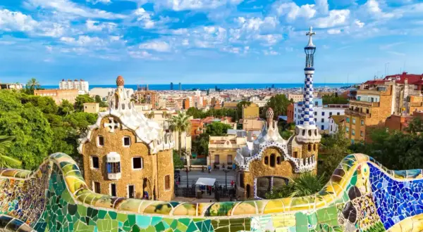 Kolorowe budowle Antonio Gaudiego w Parku Güell, Barcelona, z widokiem na miasto i morze.