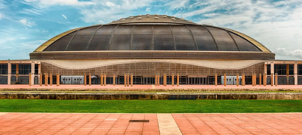 Palau Sant Jordi, z charakterystyczną kopułą, prezentuje się imponująco na tle błękitnego nieba z chmurami.