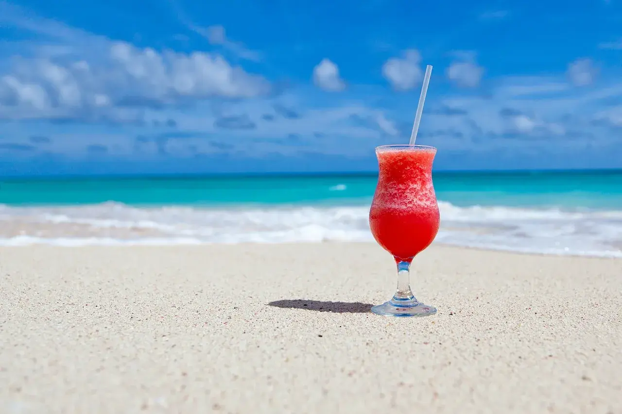 Czerwony drink na plaży, idealny do nauki słówek po hiszpańsku. Błękitne morze i piasek tworzą rajski krajobraz.