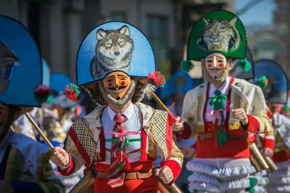 Ludzie w maskach i barwnych strojach, święta w Hiszpanii. Widać malunek wilka na kapeluszu.