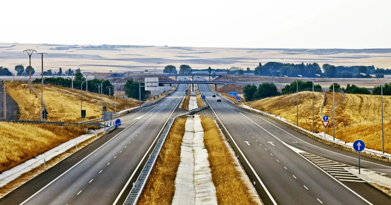 Pusta autostrada w Hiszpanii, z suchą trawą po bokach i mostami w oddali.