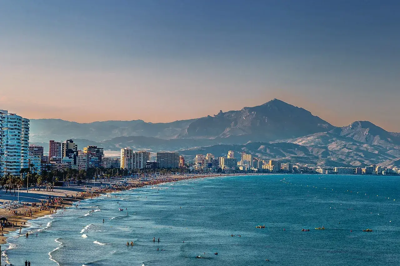 Alicante pogoda w grudniu: słoneczna plaża z ludźmi, turkusowe morze i góry w tle.