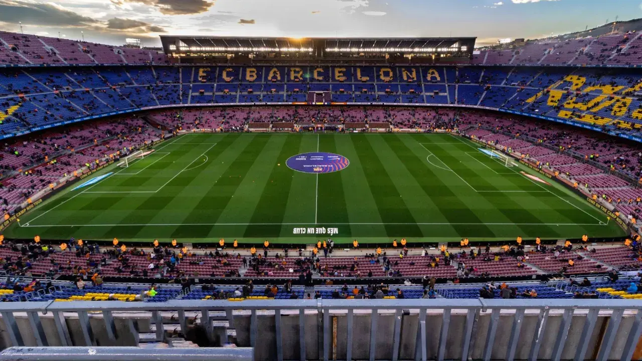 Widok na pusty stadion FC Barcelona, Camp Nou, z rzędem siedzeń w kolorach klubu i zieloną murawą.