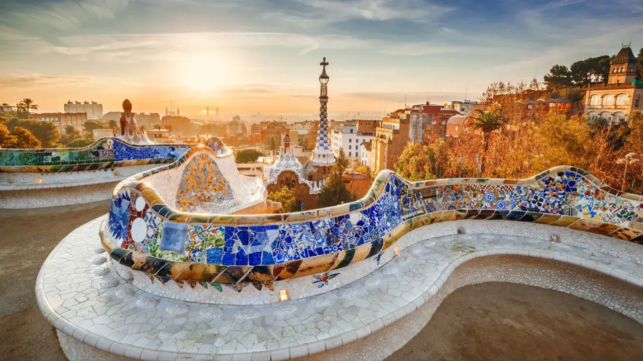 Kolorowa mozaika zdobi ławkę w Parku Güell, dziele Gaudiego. W tle widać panoramę Barcelony o zachodzie słońca.