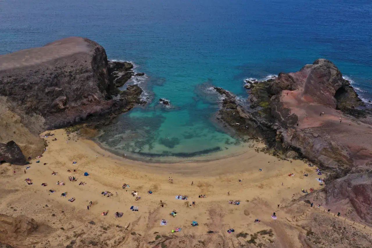 Zatoka Papagayo na Lanzarote, z turkusową wodą i piaszczystą plażą, gdzie odpoczywają turyści.