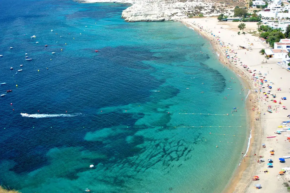 Piękne Alicante wczasy nad turkusowym morzem. Plaża pełna ludzi, łodzie na wodzie, białe klify.