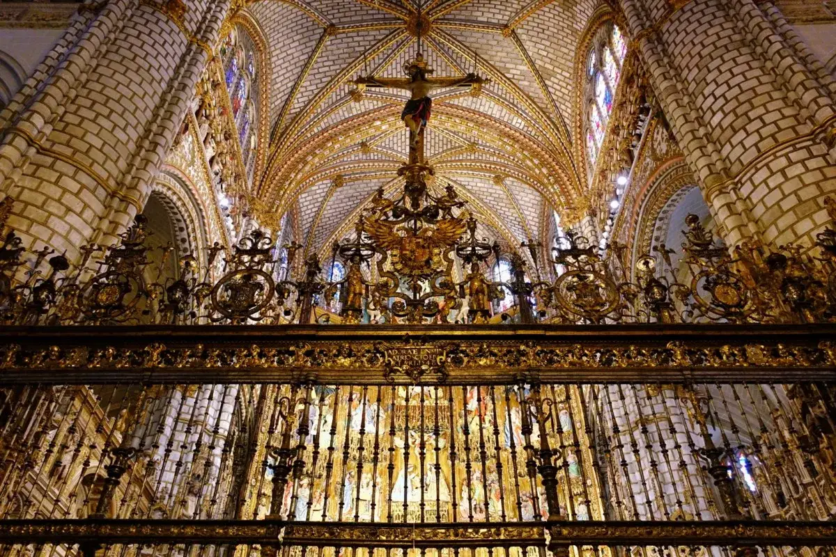 Złota krata oddziela nawę od prezbiterium w Katedrze w Toledo. Widać sklepienie, witraże i krucyfiks.