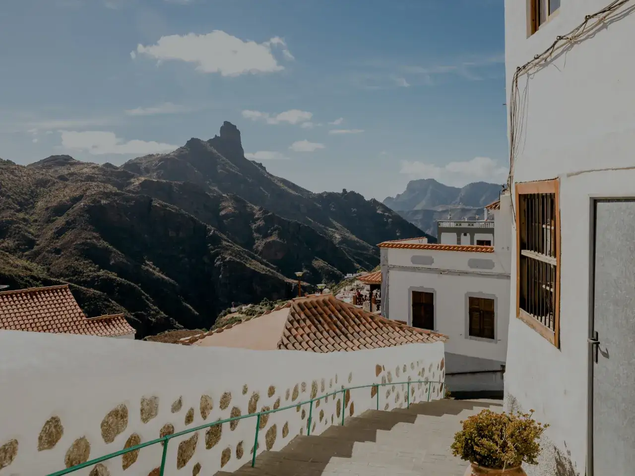 Widok na góry i białe domy w Tejeda, Gran Canaria. Kamienne schody prowadzą w dół, a zielona poręcz dodaje koloru.