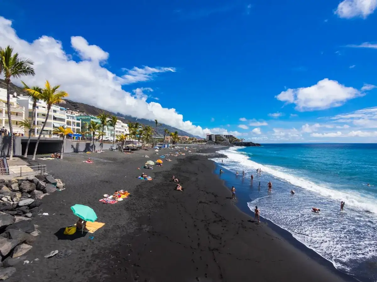 Czarne la palma plaże z turystami kąpiącymi się w oceanie i odpoczywającymi pod palmami.
