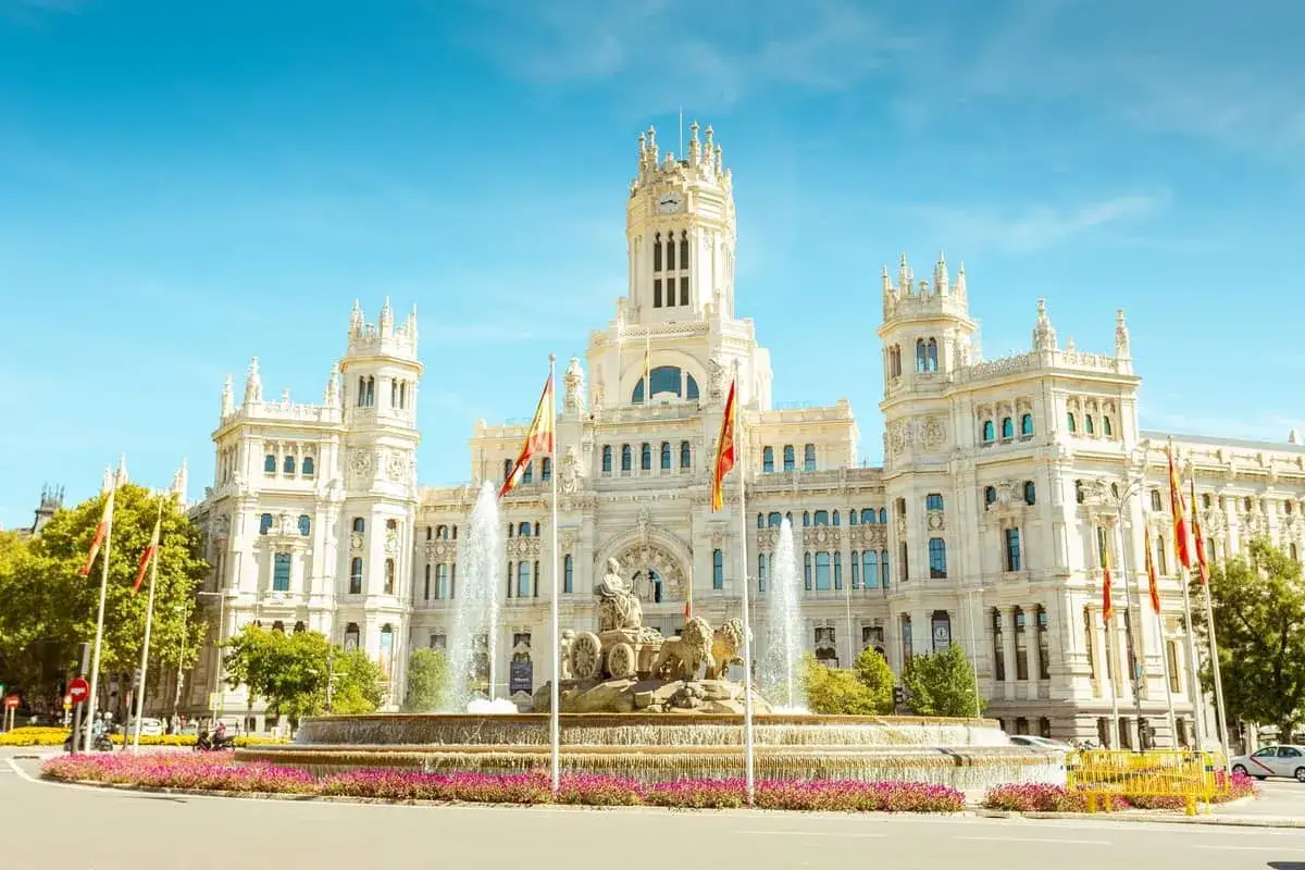 Majestatyczny budynek, dawny bank Hiszpanii, z fontanną Cibeles i hiszpańskimi flagami na placu w Madrycie.