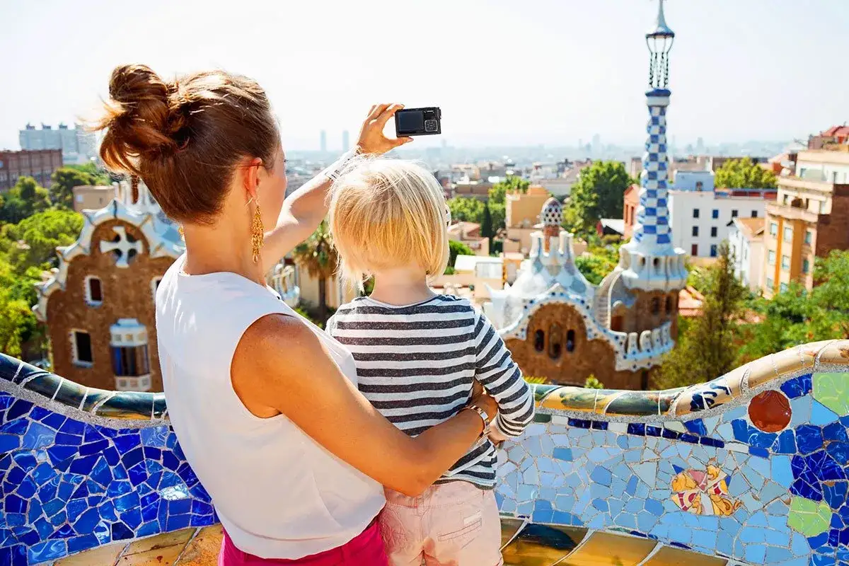Rodzina w Barcelonie z dziećmi podziwia Park Güell. Mama robi zdjęcie, a dziecko przytula się do niej.
