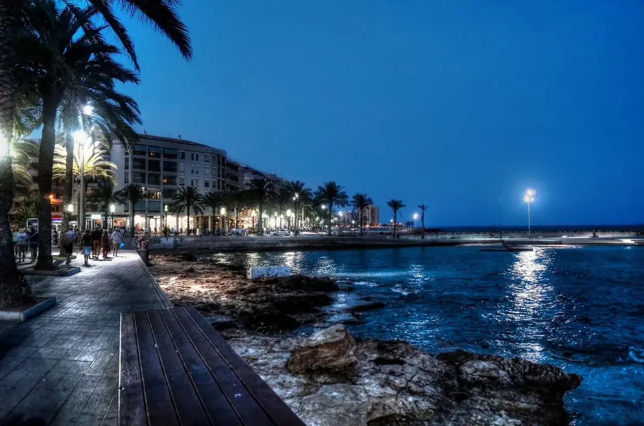 Wieczorny spacer w Torrevieja. Piękna pogoda sprzyja relaksowi nad morzem, wśród palm i oświetlonych budynków.