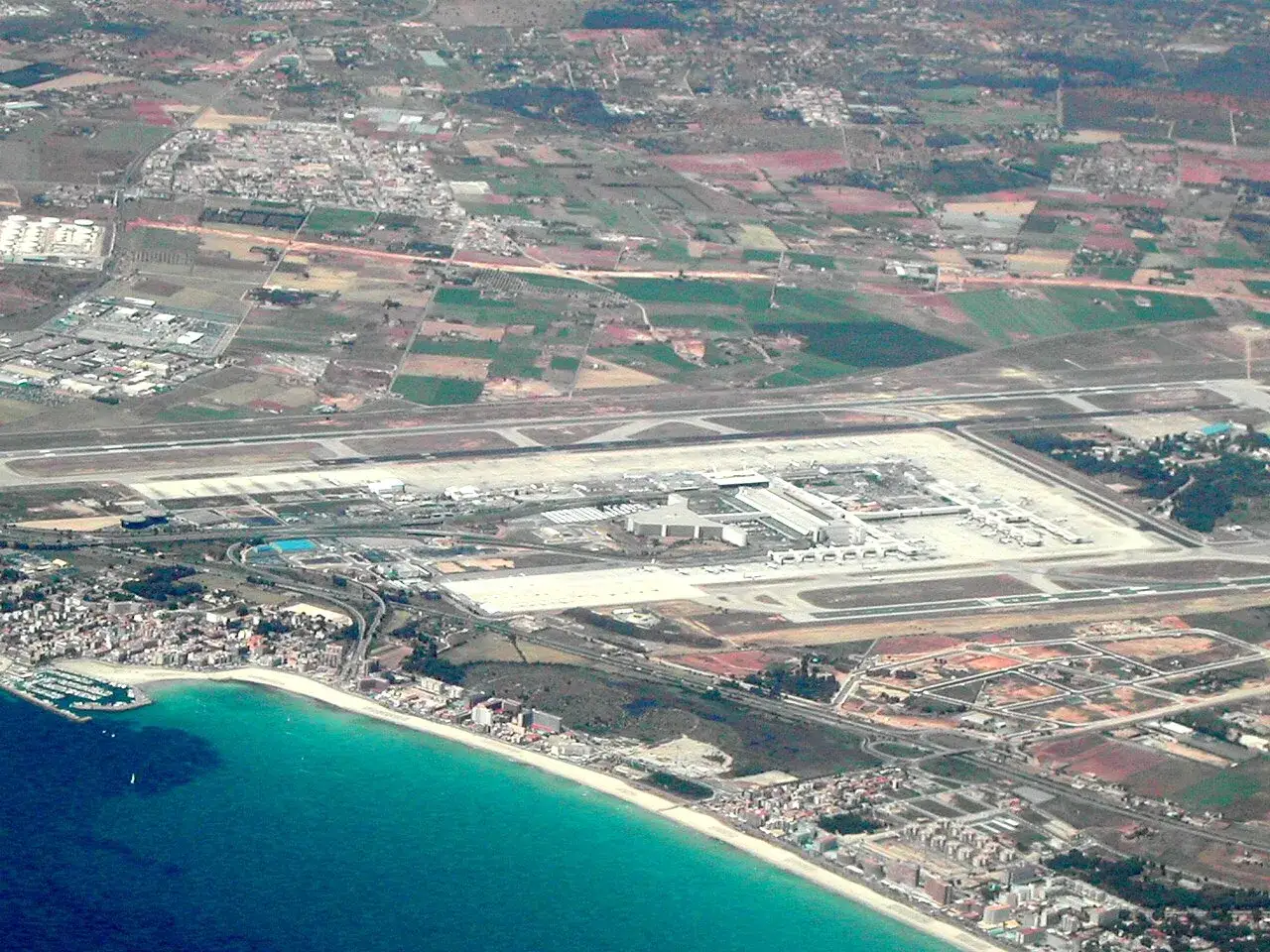 Widok z lotu ptaka na majorka lotnisko z pasami startowymi, terminalem i samolotami. W oddali widać turkusowe morze i plażę.