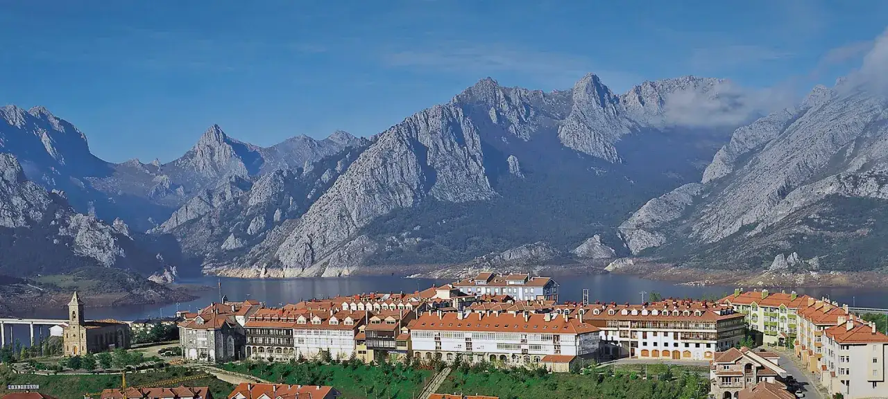 Malowniczy krajobraz z miasteczkiem nad jeziorem i skalistymi górami w tle, w regionie Leon w Hiszpanii.