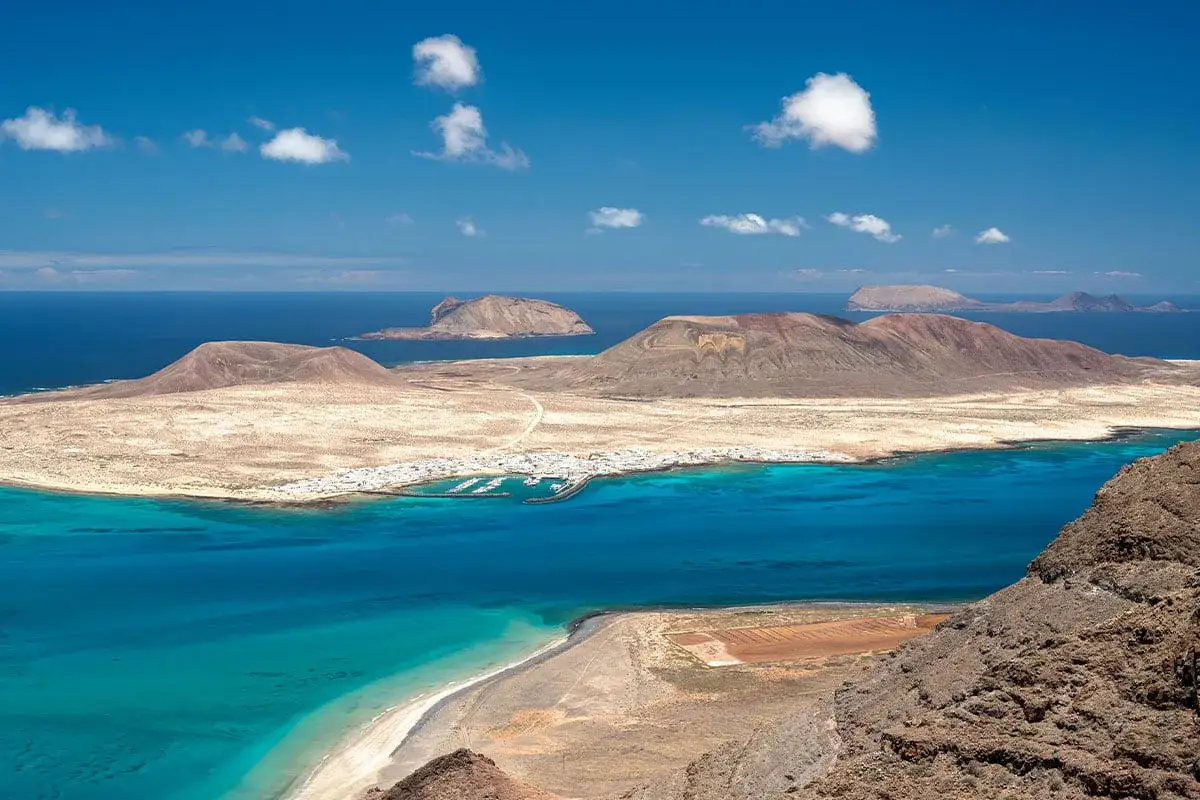Krajobraz wyspy La Graciosa, z widocznym stożkiem wulkanicznym, turkusową wodą i białymi domkami. Lanzarote wulkan.