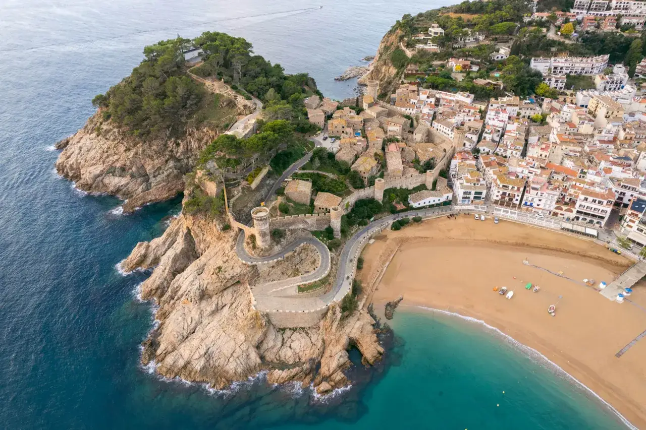 Widok z lotu ptaka na malowniczą plażę w Lloret de Mar, z krętą drogą prowadzącą do zabytkowej twierdzy na klifie.