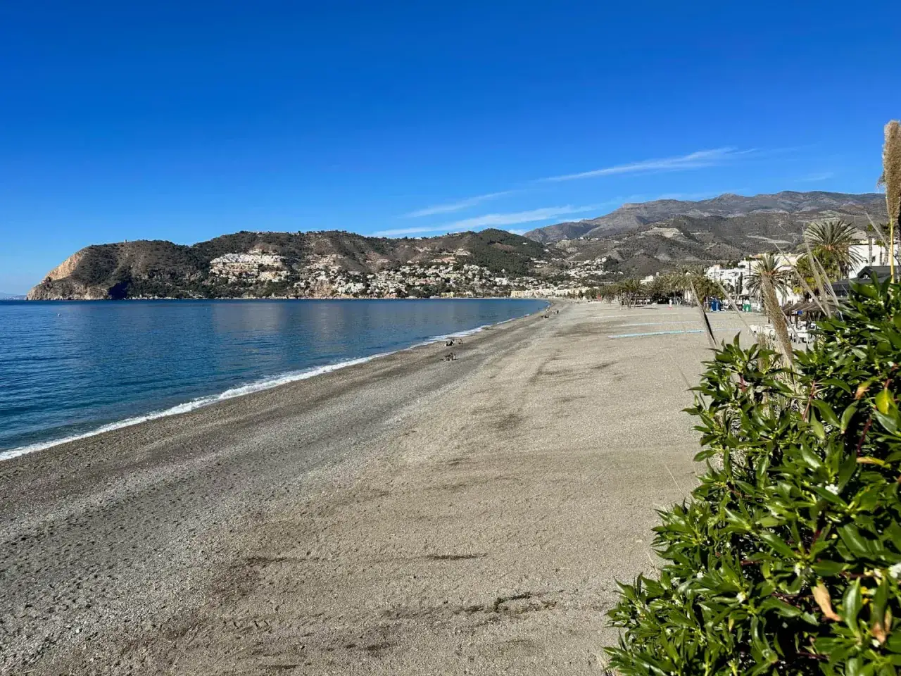 Słoneczna plaża w Hiszpanii, z widokiem na góry Sierra Nevada w oddali. Błękitne morze i piaszczysty brzeg.