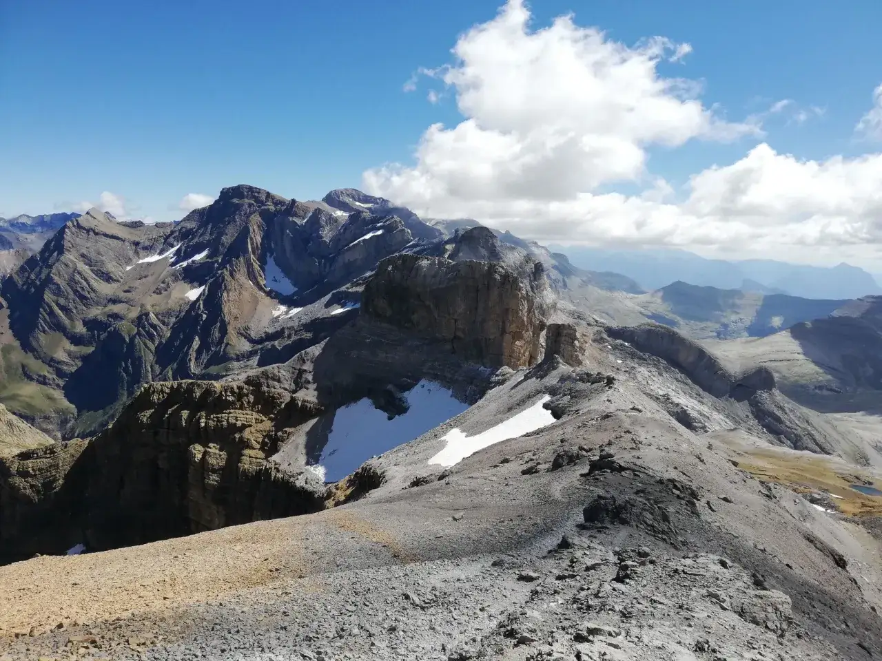 Majestatyczne szczyty Monte Perdido w Pirenejach, z ośnieżonymi zboczami i skalistymi graniami, pod błękitnym niebem z białymi chmurami.