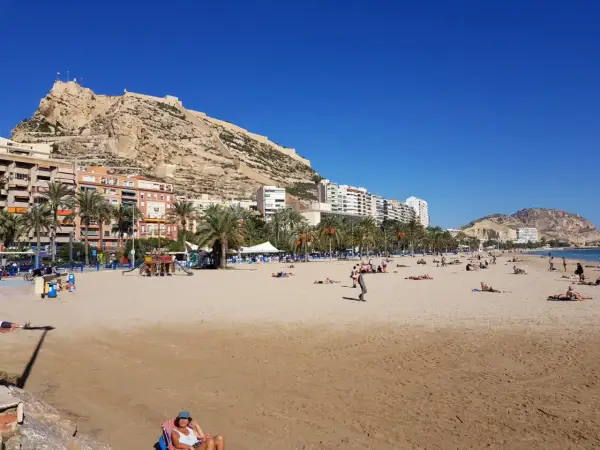 Alicante pogoda w kwietniu: słoneczna plaża z ludźmi odpoczywającymi pod zamkiem Santa Barbara.