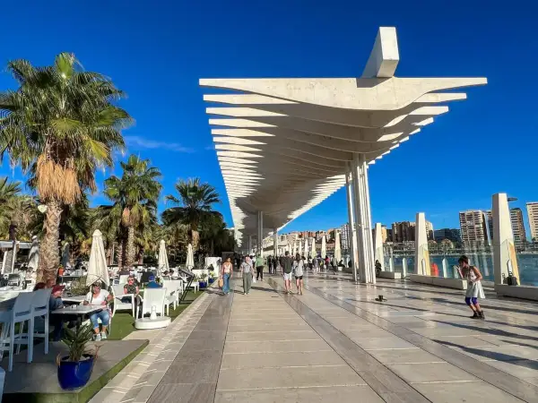 Spacerem po malaga park, pod palmami i nowoczesną pergolą, ludzie odpoczywają w kawiarniach i spacerują.