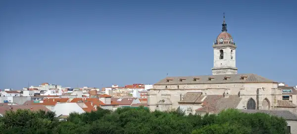 Widok na miasto Ciudad Real z kościołem i jego wieżą zegarową na tle błękitnego nieba.