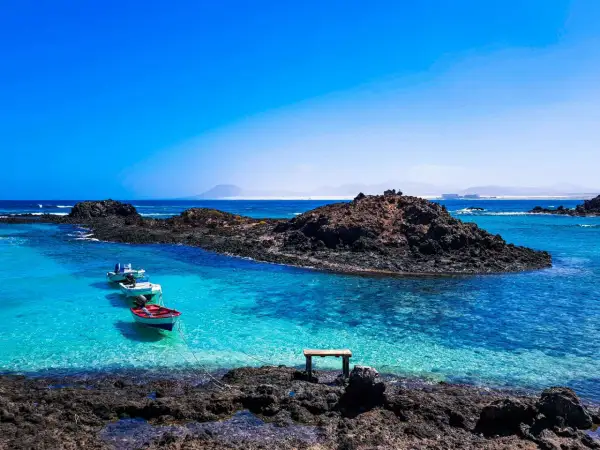 Fuerteventura w lutym: spokojne, turkusowe morze, skaliste wybrzeże i łodzie kołyszące się na falach. Idealna pogoda na relaks.