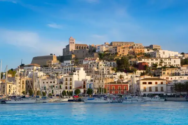 Widok na port z żaglówkami i wzgórzem z białymi domami i katedrą. Ibiza atrakcje zachwycają!