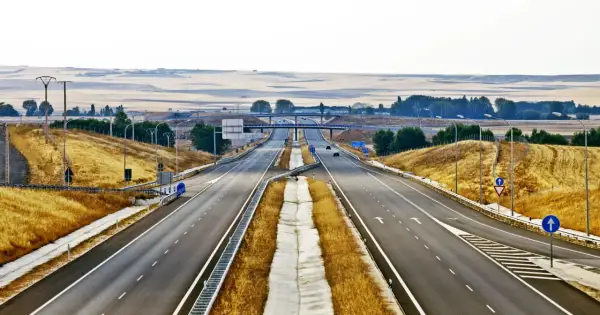 Pusta autostrada w Hiszpanii, z suchą trawą po bokach i mostami w oddali.