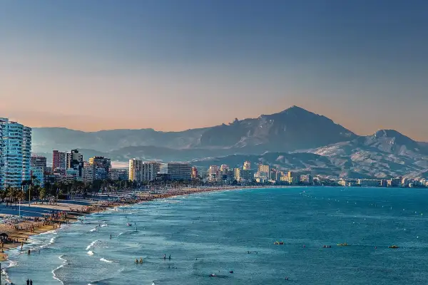 Alicante pogoda w grudniu: słoneczna plaża z ludźmi, turkusowe morze i góry w tle.