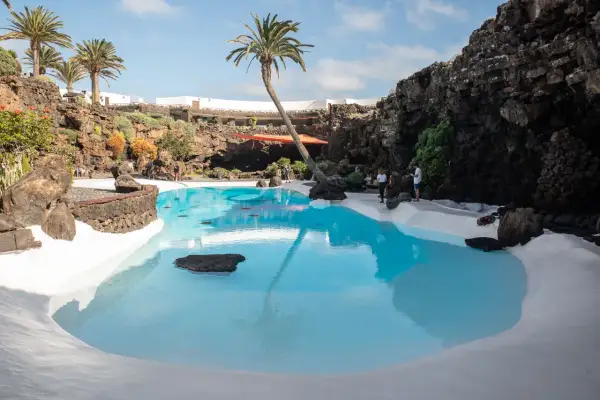 Basen w otoczeniu wulkanicznych skał na Lanzarote, z palmą pochyloną nad turkusową wodą.
