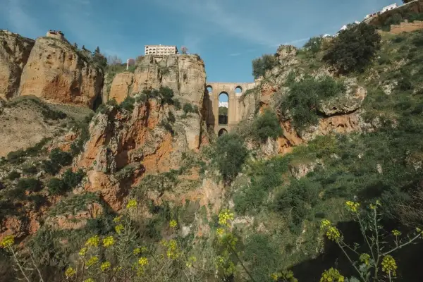 Mosty w Ronda, Andaluzja najpiękniejsze miejsca. Imponująca architektura na tle skalistych zboczy, porośniętych zielenią i żółtymi kwiatami.